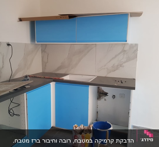 מטבח בשיפוץ עם ארונות כחולים, כיור ודלי צבע